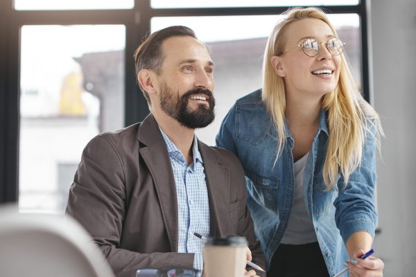 Two business partners look attentively at presentation of full screen, being glad meet together, focused into distance, going to have coffee break. Creative copywriters collaborate for common project